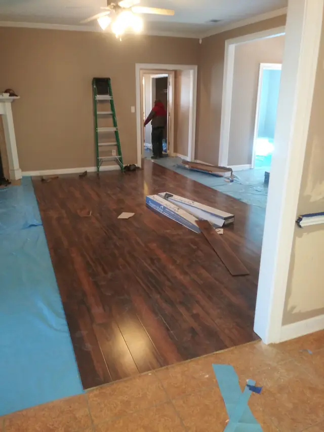Laminate planks part-laid over a protective sheet, with a worker behind