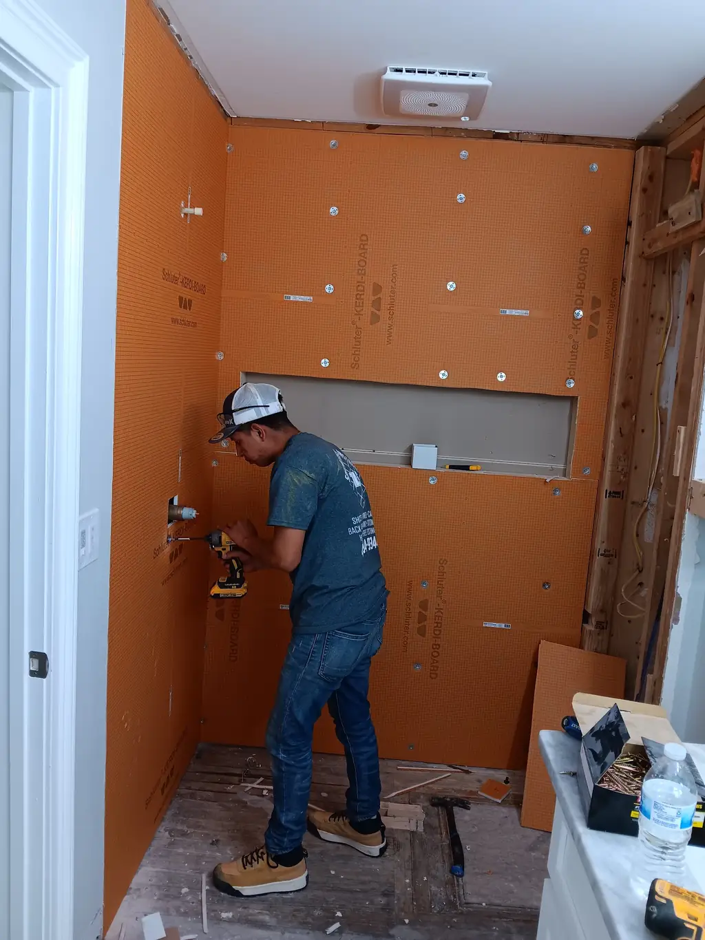 A crew member fitting Schluter KERDI-BOARD panels onto the shower walls during a rebuild, before any tile