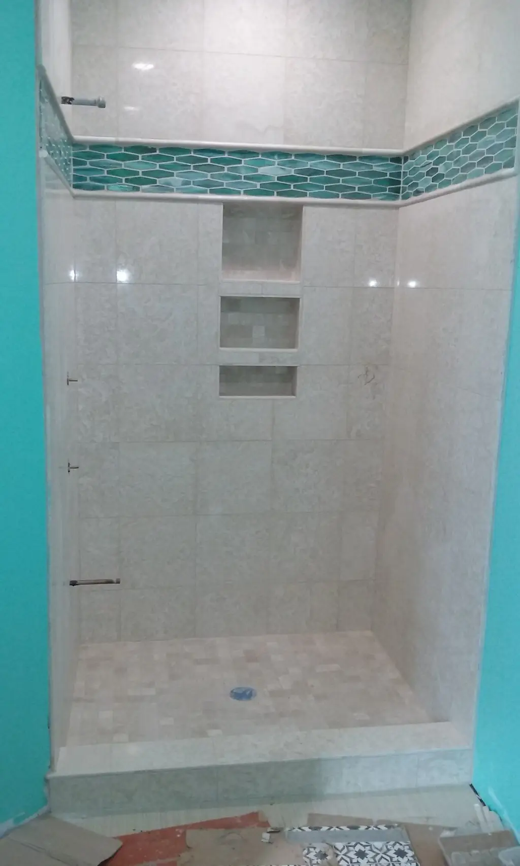 Finished tiled shower: travertine-look field tile, a teal glass hex band and three stacked niches over a tiled pan